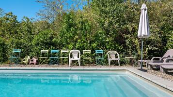 Une piscine entourée d’une végétation luxuriante, avec des chaises longues et des parasols.