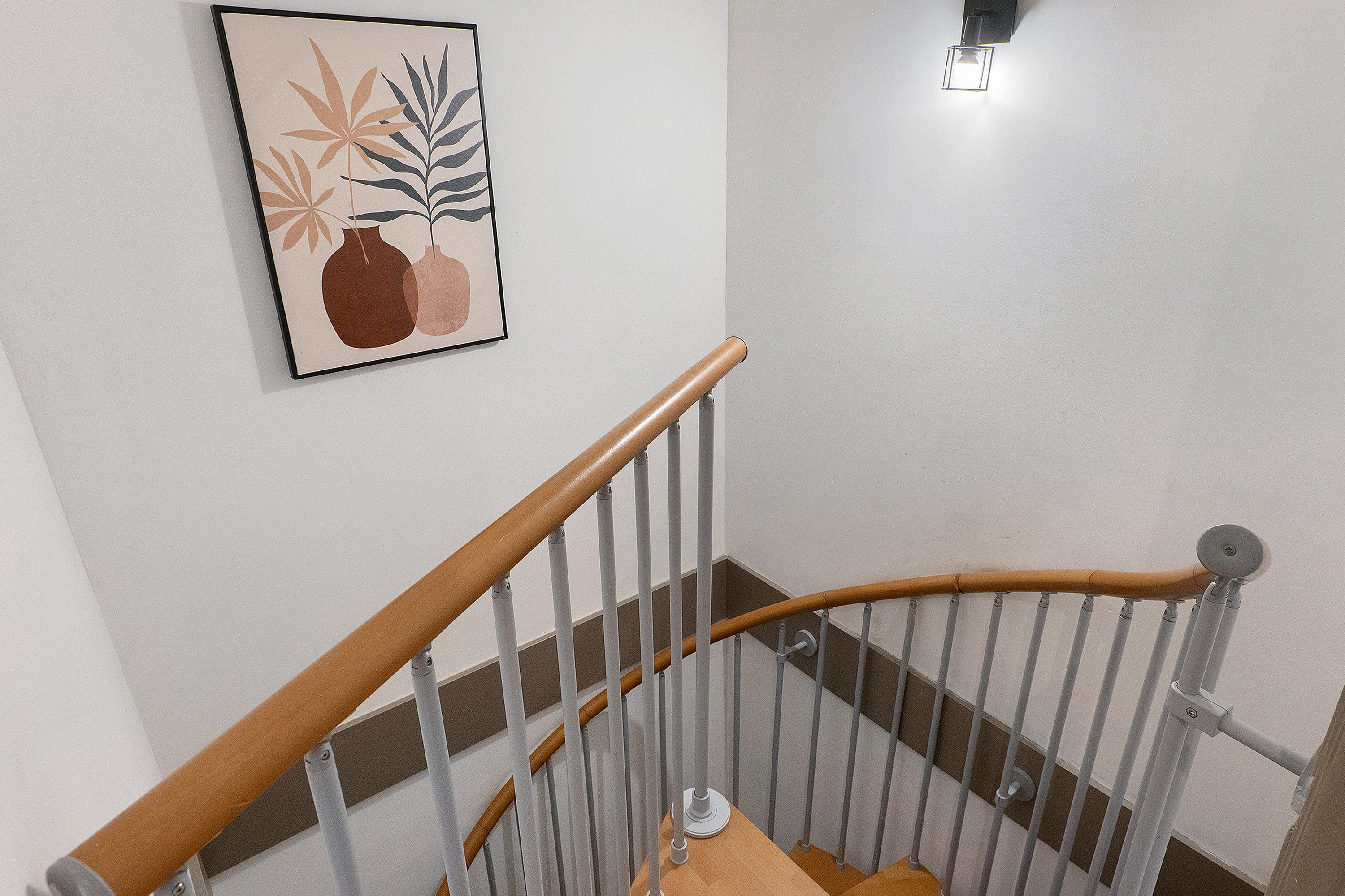 Un escalier avec des rampes en bois et des balustrades en métal, menant à un palier où est accrochée une œuvre d’art encadrée au mur.