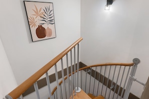 En trappa med träräcken och metallspjälor, som leder upp till en liten plattform där ett inramat konstverk hänger på väggen.