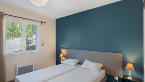 A bedroom with a bed, two bedside tables with lamps, a window with curtains, and a radiator. - Villa 'Gite Les Bouches Rouges 6 Personnes' with Mountain View, Wi-Fi and Air Conditioning (Vesseaux)