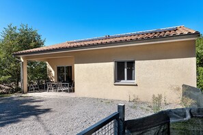 A building with a tiled roof, a covered patio with chairs, and a gravel ground. - Villa 'Gite Les Bouches Rouges 6 Personnes' with Mountain View, Wi-Fi and Air Conditioning (Vesseaux)