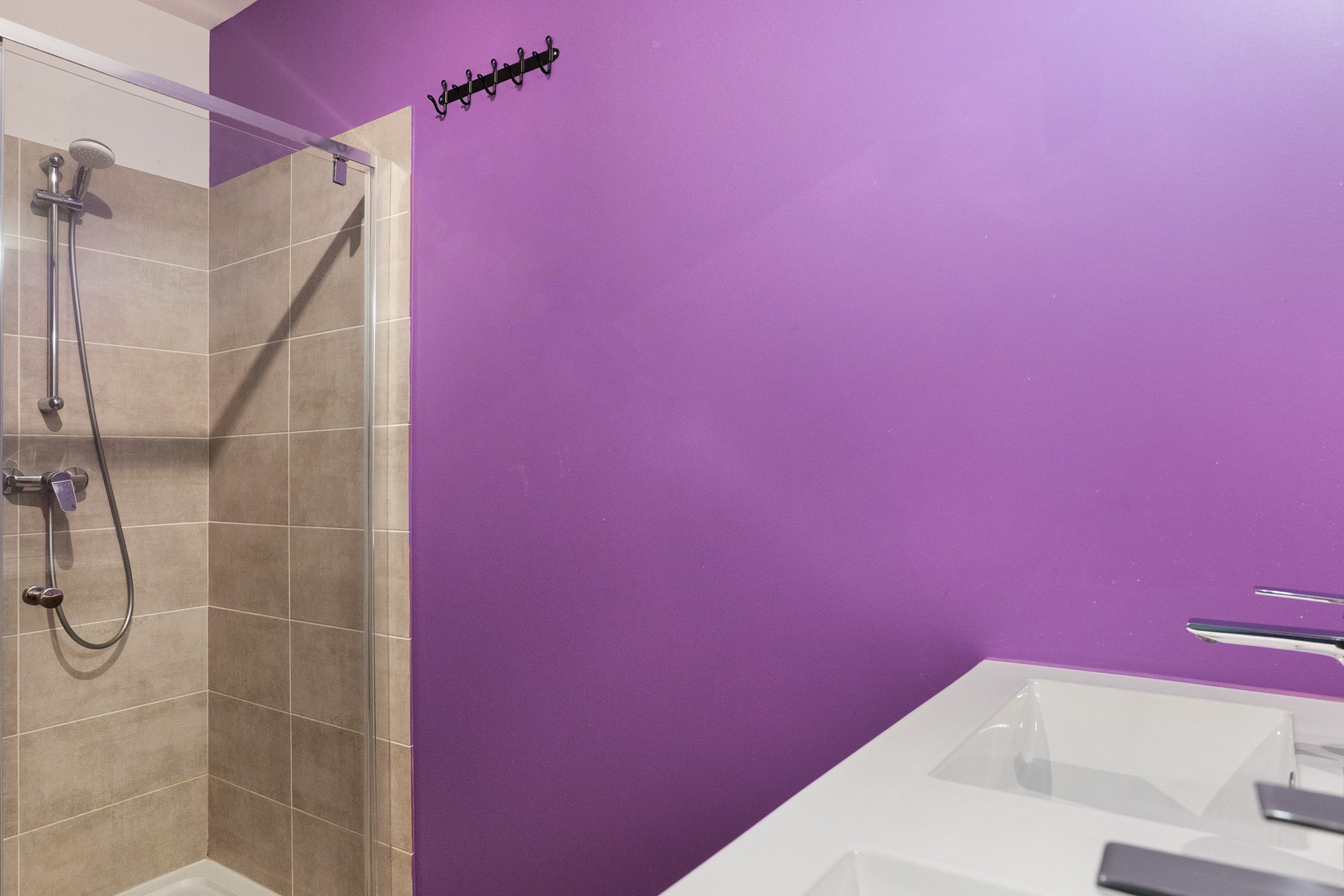 Une salle de bain avec une douche, un lavabo et un mur violet.