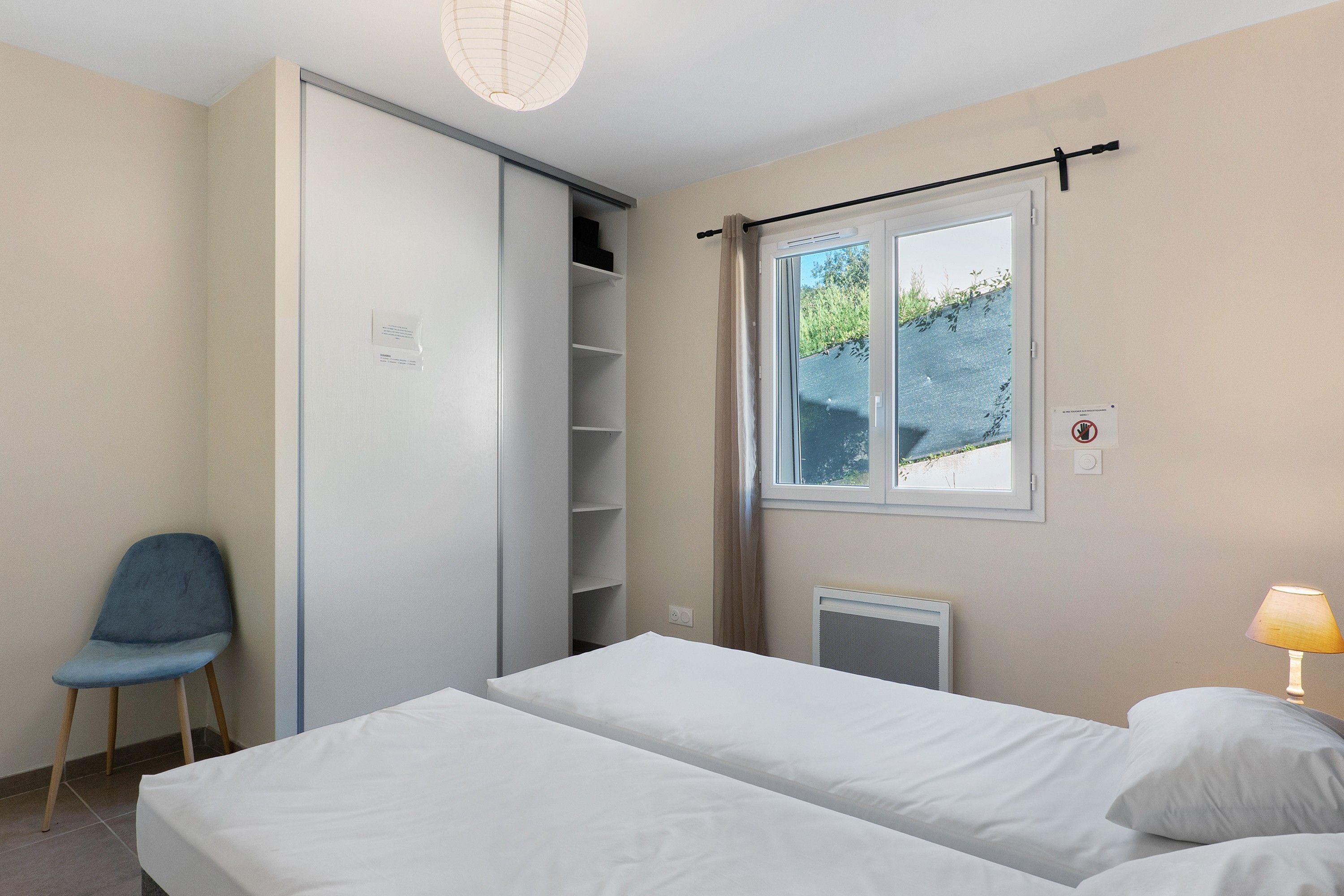 Une chambre à coucher avec un lit, une chaise, une armoire, une fenêtre donnant sur un beau paysage et une lampe.