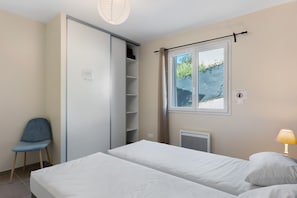 Un dormitorio con cama, una silla, un armario, una ventana y una lámpara.