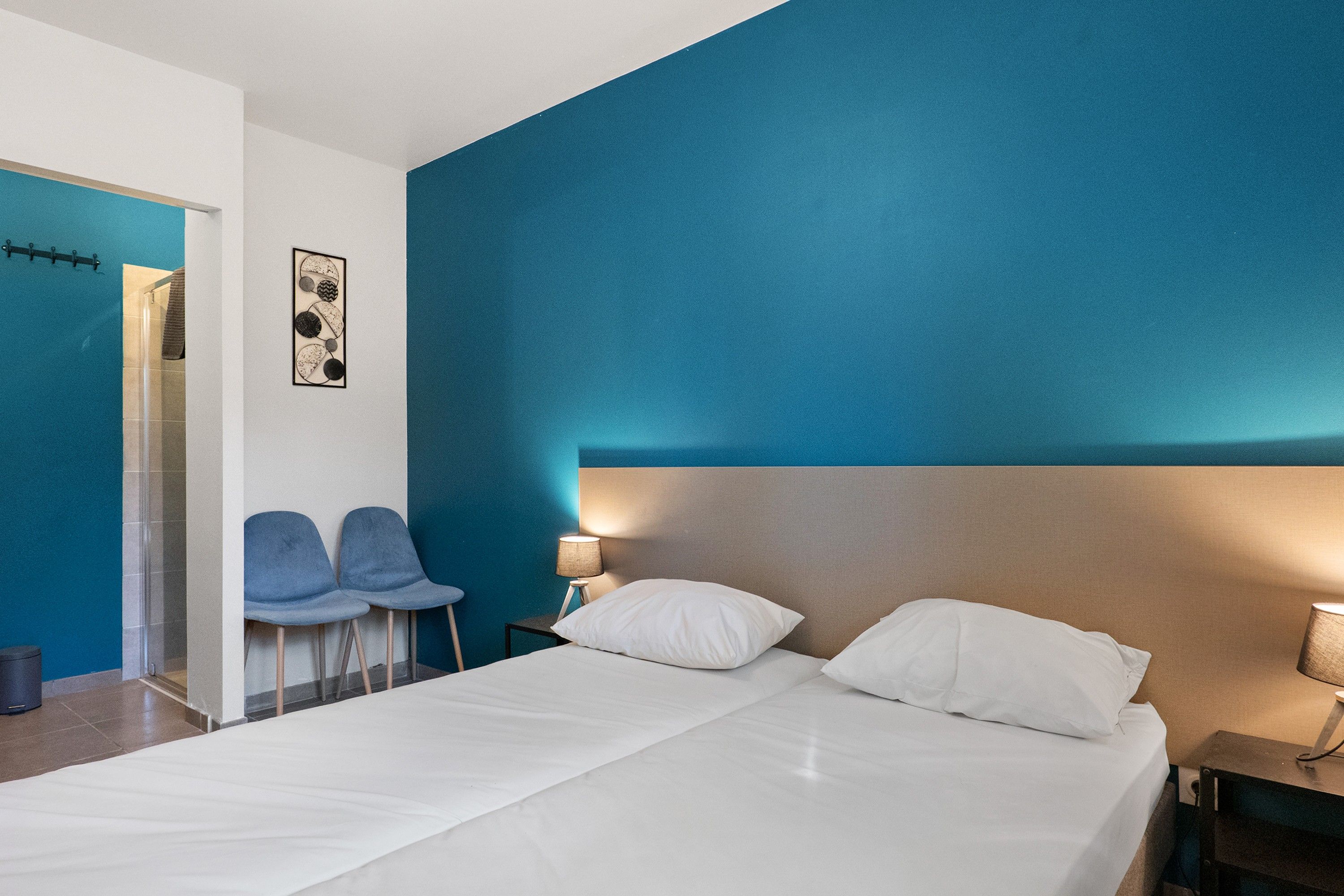 Una habitación de hotel con cama, mesita de noche, lámpara y una obra de arte en la pared.