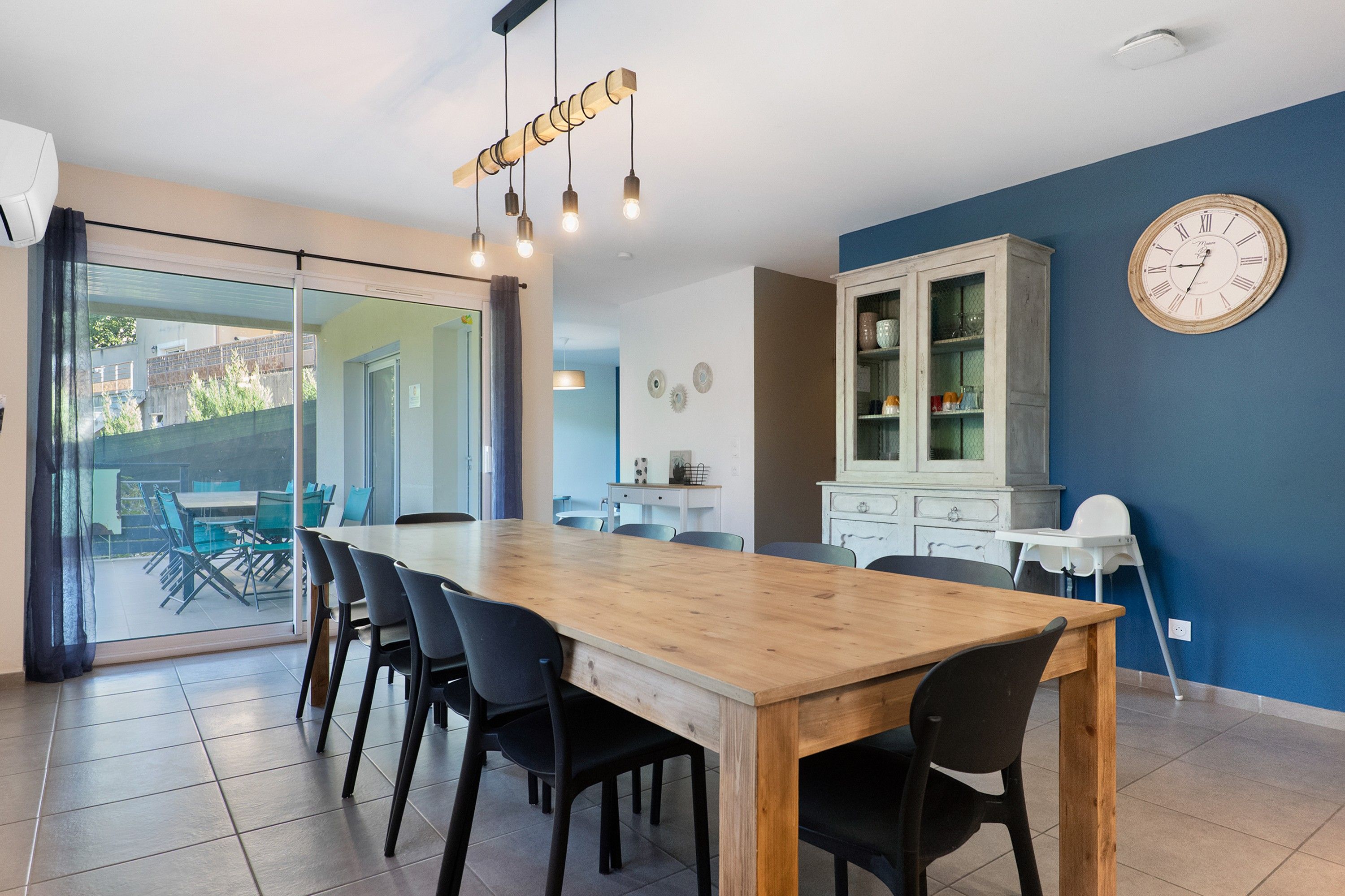 Un coin repas avec une table et des chaises en bois, un meuble avec des portes en verre et une horloge murale.