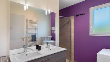 Une salle de bain avec un double lavabo, un miroir, un porte-serviettes, une douche et une fenêtre.