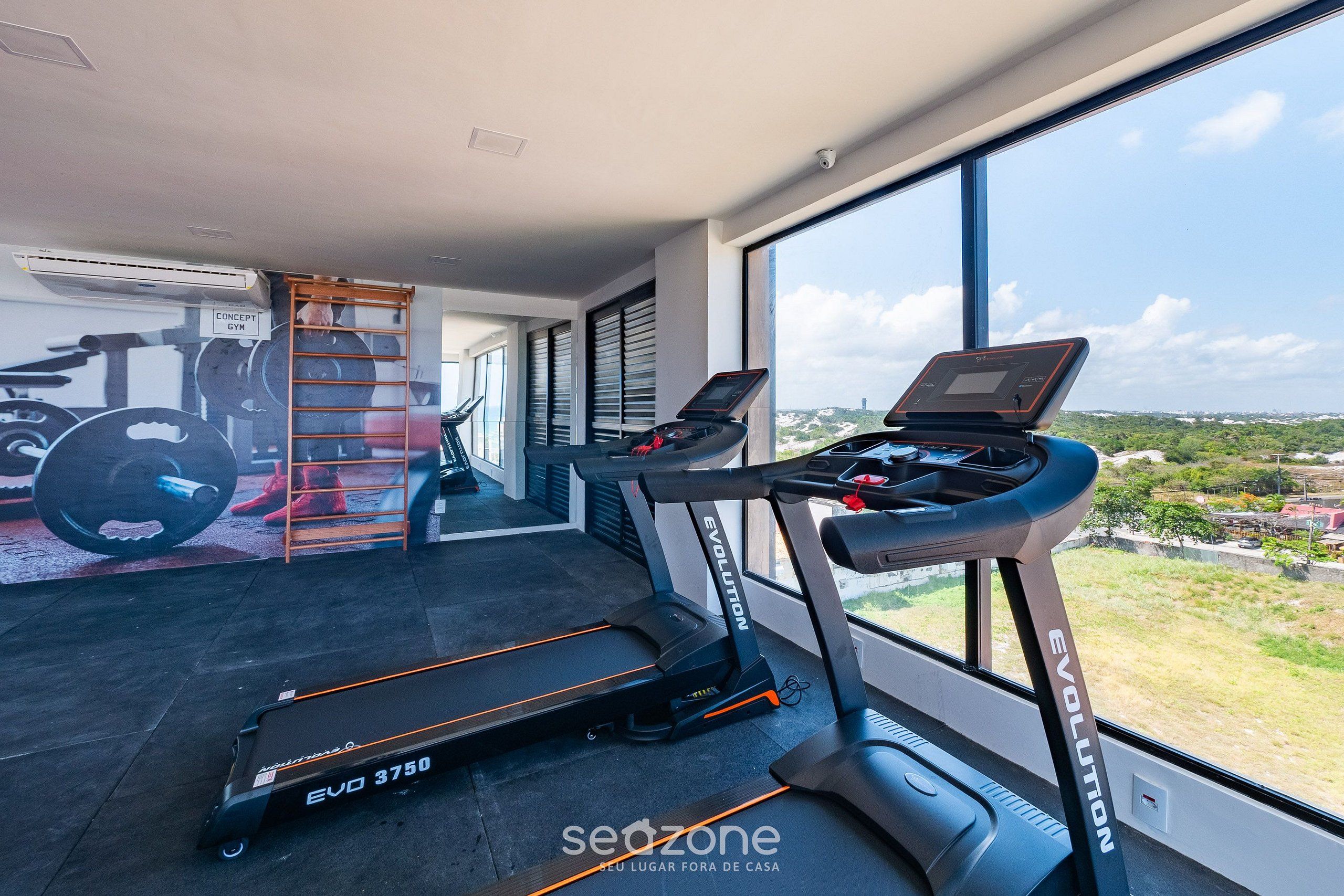 Une salle de sport équipée de tapis de course, d’un climatiseur fixé au mur et d’une grande fenêtre donnant sur l’extérieur.