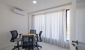 A conference room with a table, four chairs, a white air conditioning unit, and a window with white curtains. - Fully Equipped Apartments in a Building With a Pool and Gym, 280m From the Beach - Clfs (Salvador)
