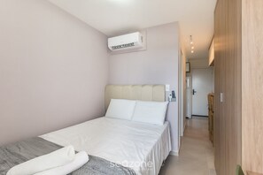 A bedroom with a bed, a wall-mounted air conditioner, and a hallway leading to a bathroom. - Fully Equipped Apartments in a Building With a Pool and Gym, 280m From the Beach - Clfs (Salvador)