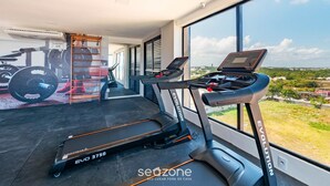 Une salle de sport à domicile équipée de tapis de course, d’un banc de musculation et d’un mur orné d’illustrations d’appareils de fitness.