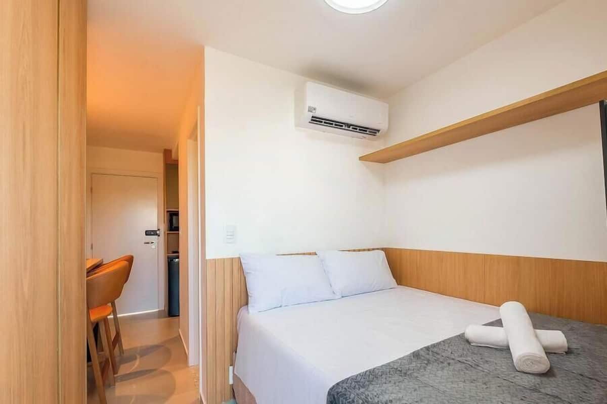 A hotel room with a bed, a desk, and an air conditioning unit.