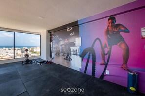 Un gimnasio con un ventanal grande, equipo de ejercicio y un mural de una persona haciendo ejercicio.