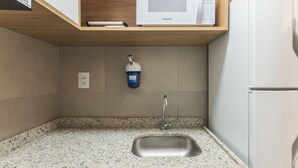 Egy konyha gránit munkalappal, rozsdamentes acél mosogatóval és egy mikrohullámú sütővel, mely egy fa polcon található.