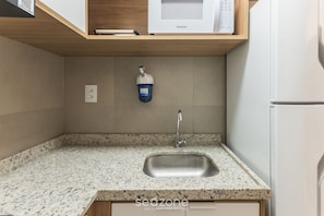 Una cocina con encimera de granito, pileta de acero inoxidable y un microondas sobre una repisa de madera.