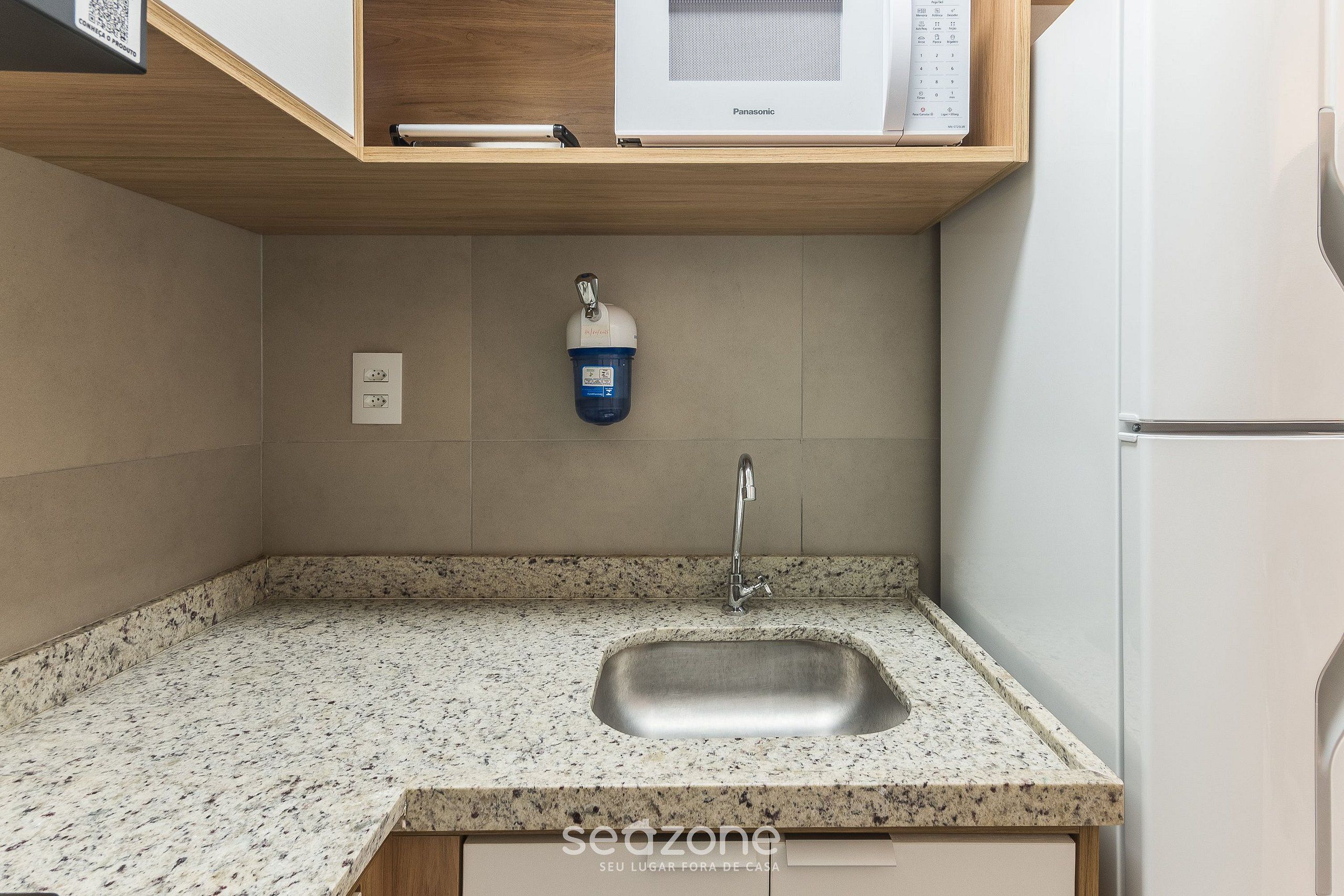Cozinha com bancada de granito, pia de aço inoxidável e micro-ondas em prateleira de madeira.