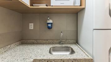 Cozinha com bancada de granito, pia de aço inoxidável e micro-ondas em prateleira de madeira.