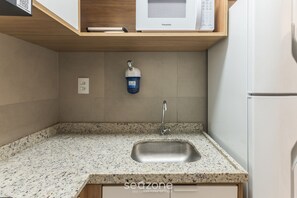 Une cuisine dotée d’un plan de travail en granit, d’un évier en acier inoxydable et d’un four à micro-ondes posé sur une étagère en bois.