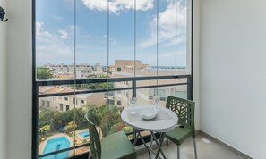 Un balcon avec une table et des chaises, donnant sur une piscine et des immeubles.