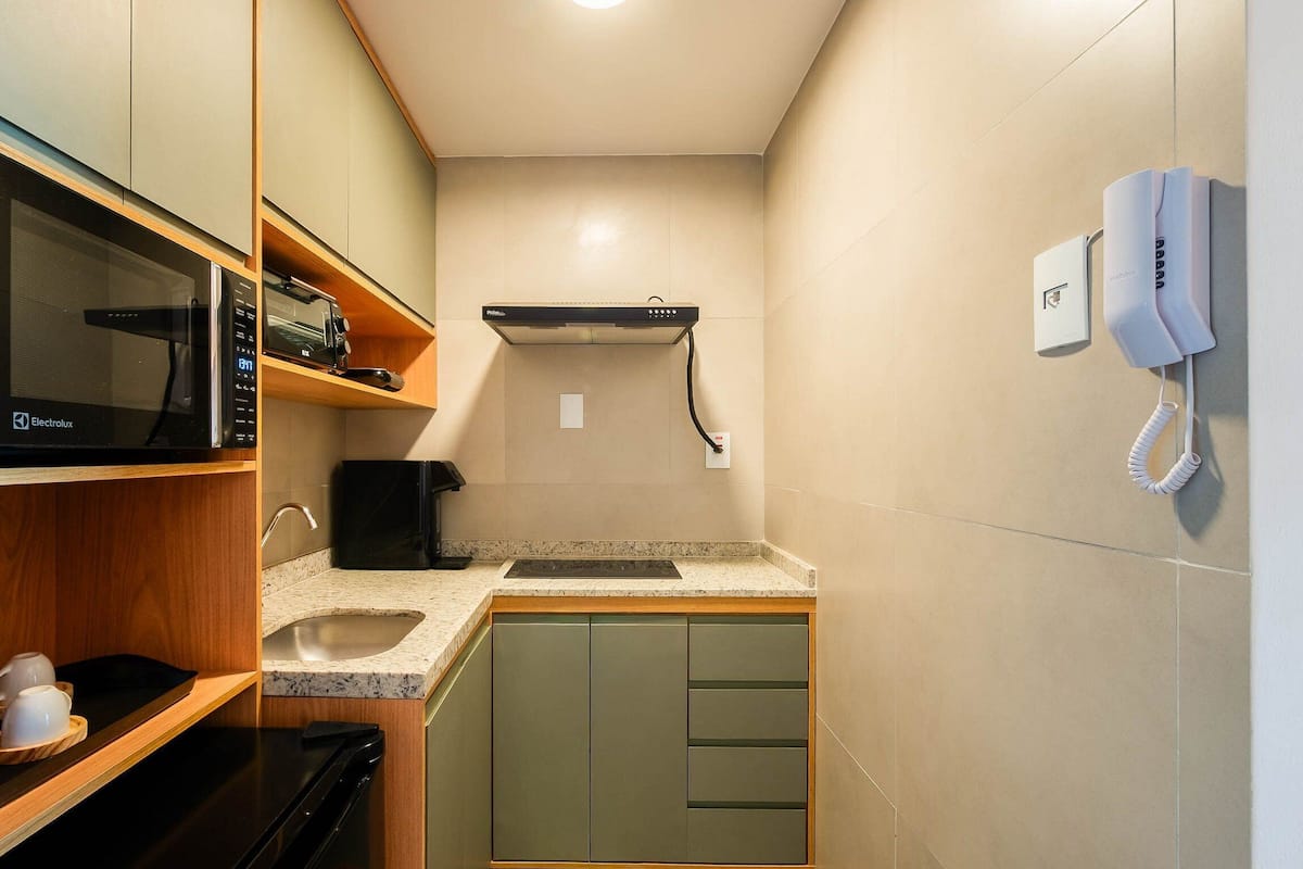A compact kitchenette with a microwave, toaster, and coffee maker on the countertop, a sink, and a telephone mounted on the wall.