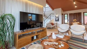 Un salon moderne doté d’un téléviseur à écran plat, d’un meuble de rangement en bois, de fauteuils blancs et d’un tapis rayé aux couleurs vives.