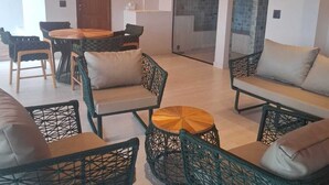 Un vaste espace de vie aménagé avec des meubles en osier, une table basse ronde et une table à manger avec des chaises.