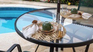 Une table ronde en verre, surmontée d’un set de table en fibres tressées, une théière verte, un verre et une serviette blanche.