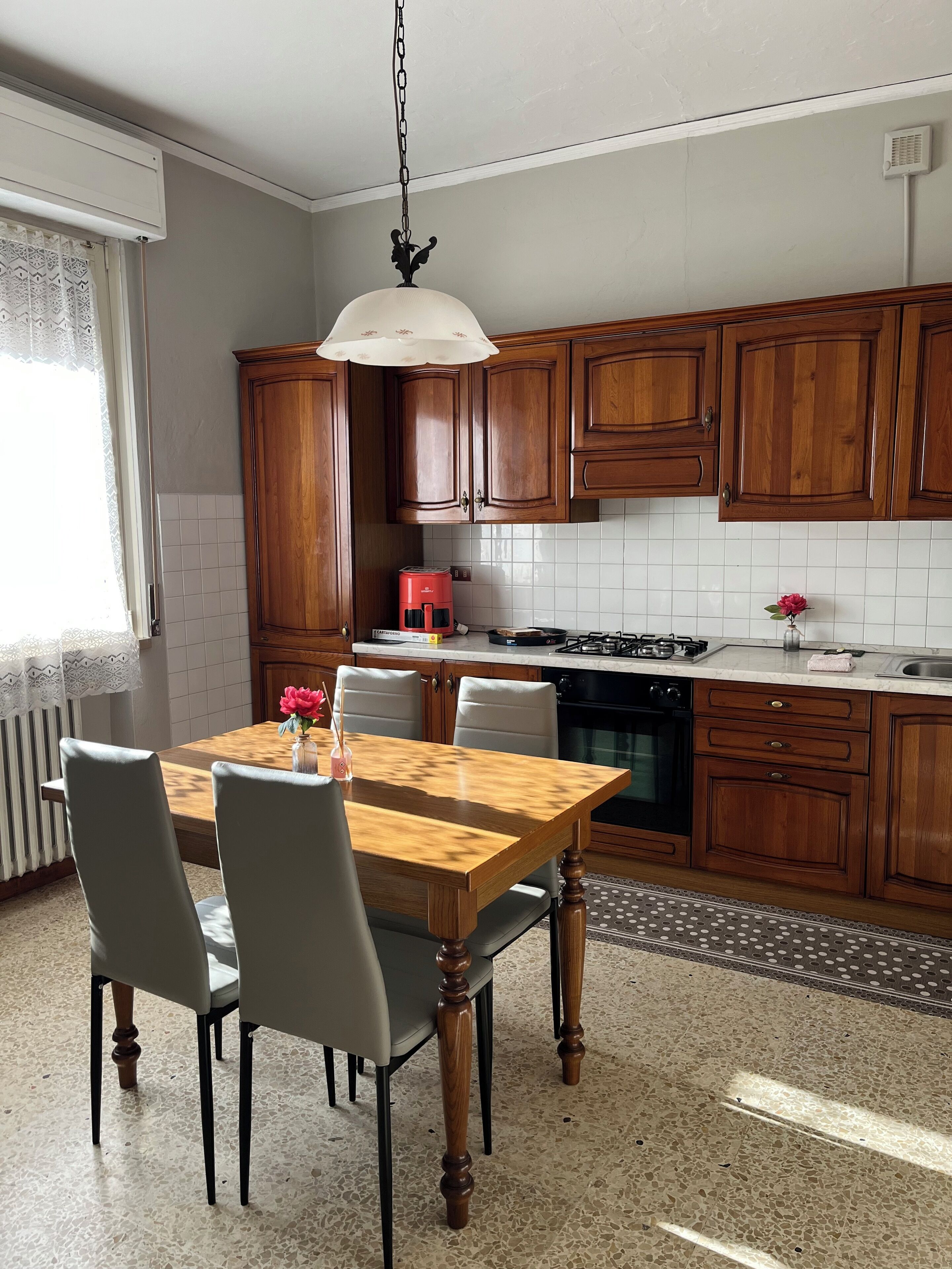 Una cucina con mobili in legno, un tavolo da pranzo con sedie, un lampadario e uno schienale piastrellato.