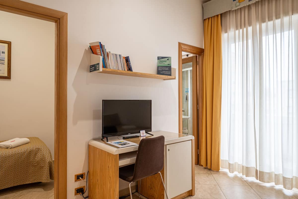 Ein Hotelzimmer mit Schreibtisch, Stuhl, Fernseher, Bücherregal und einem Bett.