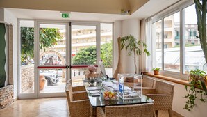 A hotel room with a glass table, wicker chairs, a potted plant, and a view of the street through a glass door. - Hotiday Gallipoli Centro (Gallipoli)