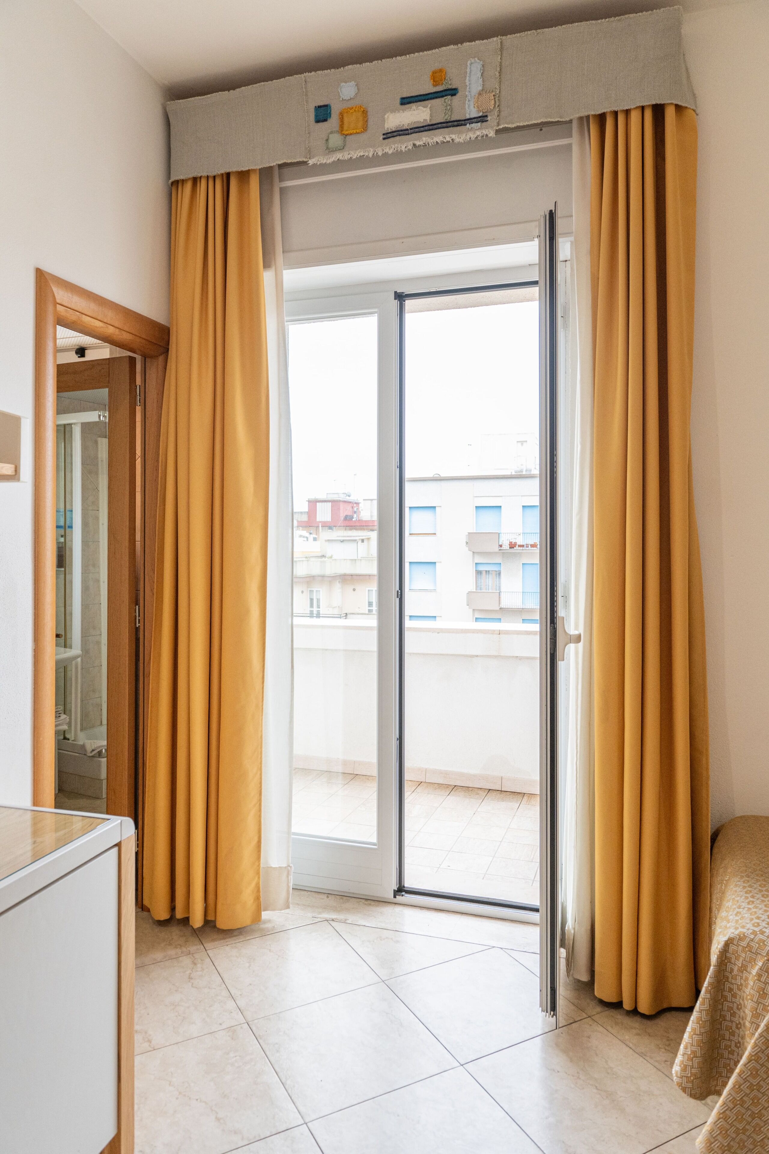 Una habitación con puerta corrediza de vidrio que da a un balcón, una cama y una mesita.
