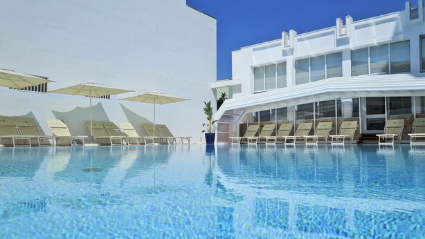 A swimming pool with lounge chairs and umbrellas, a modern building with large windows, and a clear blue sky. - Hotiday Gallipoli Centro (Gallipoli)