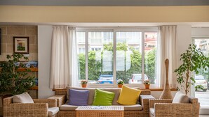 A room with wicker furniture, a window with curtains, and potted plants. - Hotiday Gallipoli Centro (Gallipoli)
