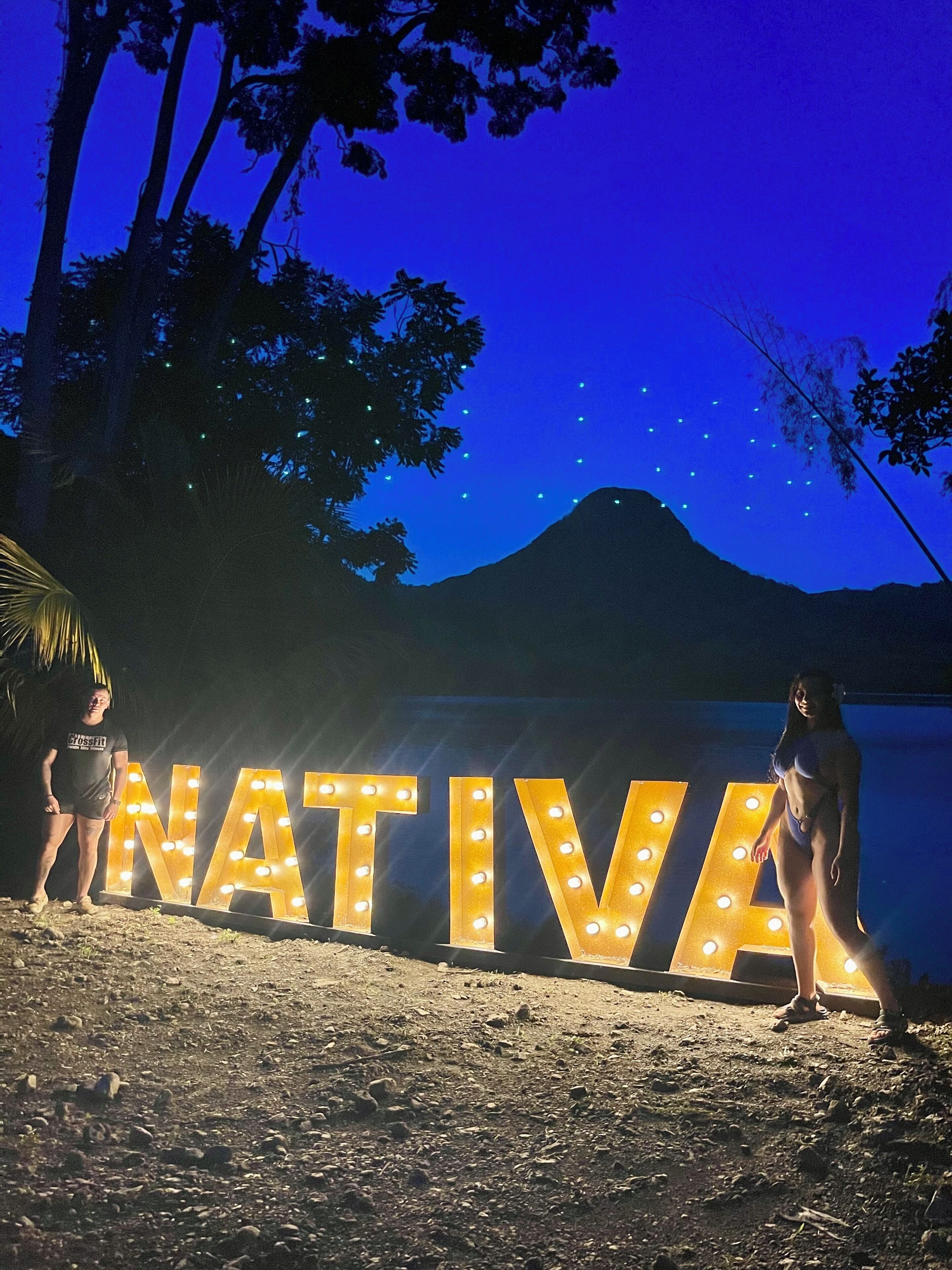 A beach with large illuminated letters spelling "NATIVA" and a mountain in the background.