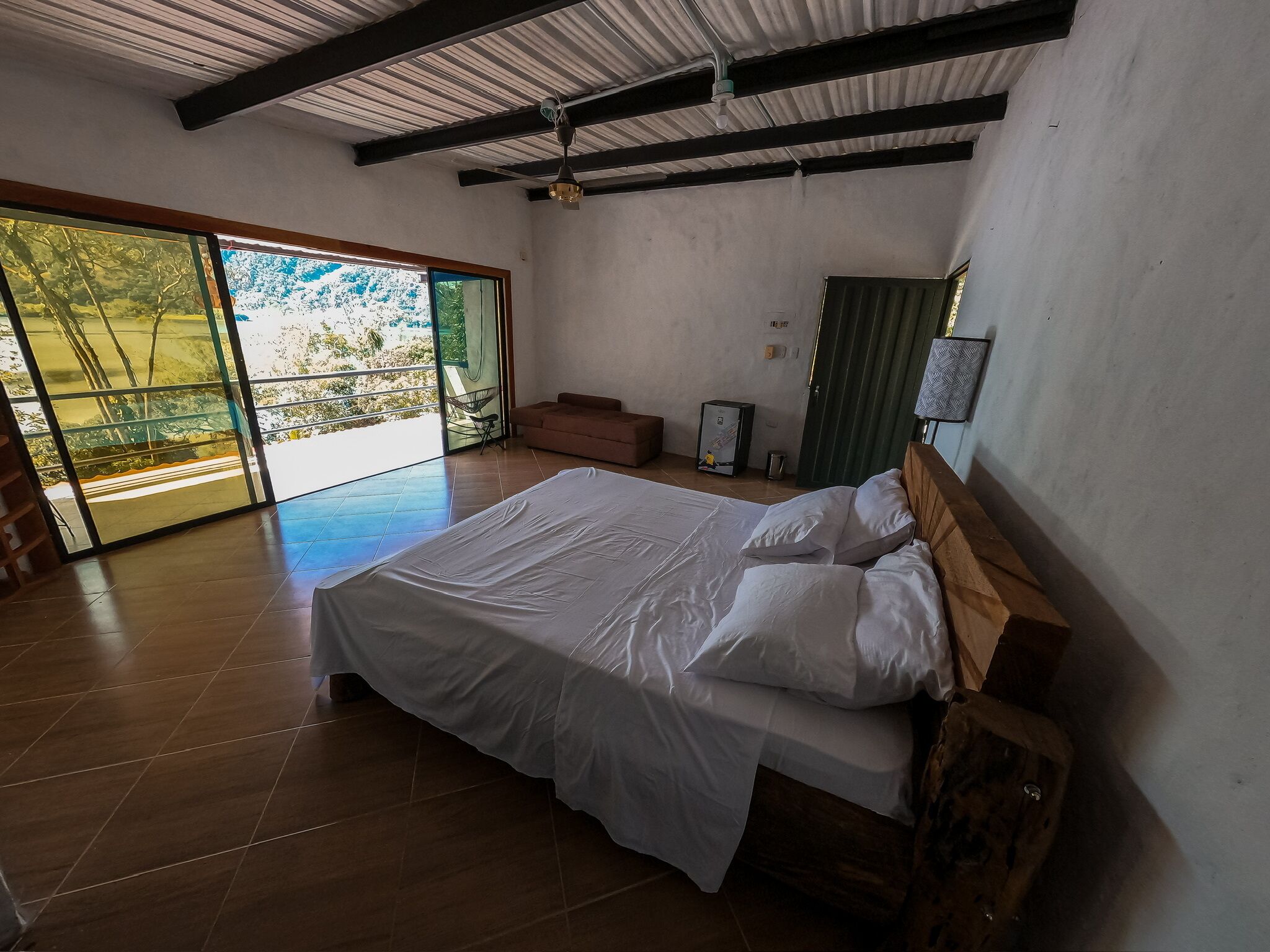 Un dormitorio moderno con una cama grande, un ventanal corredero que da a un balcón y un ventilador de techo.