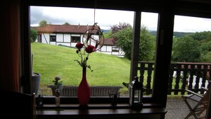 A view from a window with a red vase, a small potted plant, and a metal basket on a windowsill. - Bungalow 21 on the edge of the forest with terrace and view of the Wasserkuppe. (Dipperz)