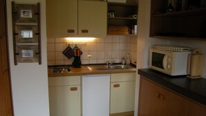 A compact kitchen with a dishwasher, a microwave, and a sink. - Bungalow 21 on the edge of the forest with terrace and view of the Wasserkuppe. (Dipperz)