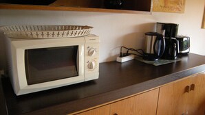 A microwave oven on a wooden countertop with a coffee maker and a kettle. - Bungalow 21 on the edge of the forest with terrace and view of the Wasserkuppe. (Dipperz)