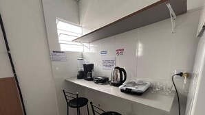 A small kitchenette with a coffee maker, kettle, and a scale. There are two black bar stools and a window above the counter. - Studio triplo na Vila Guilherme SP  (São Paulo)
