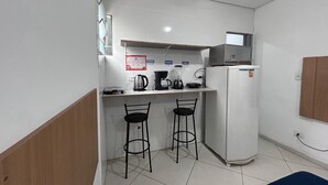 A compact kitchenette with two bar stools, a refrigerator, a coffee maker, and a kettle. - Studio triplo na Vila Guilherme SP  (São Paulo)
