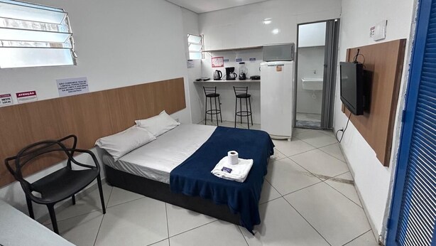 A hotel room with a bed, a desk, a chair, a kitchenette, and a TV. - Studio triplo na Vila Guilherme SP  (São Paulo)