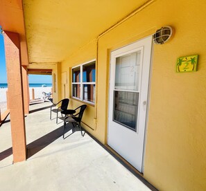 A covered outdoor area with a yellow wall, a door with a number, and two windows.