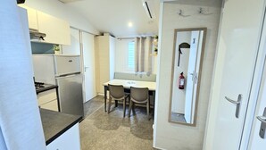 A compact kitchen with a refrigerator, a dining table with chairs, and a mirror on the wall. - ⛱️ Direct beach access - 4* campsite All-comfort mobile home + Covered terrace (Vias)