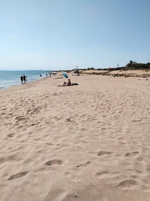Una amplia playa de arena con huellas de pasos y algunas personas caminando.