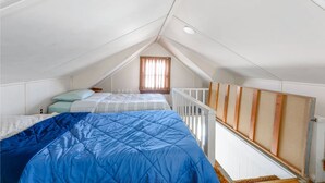 Un pequeño dormitorio en el ático con dos camas, una ventana con cortinas y techo blanco.