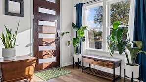 A wooden door with a glass panel, a bench, potted plants, and a window with curtains.