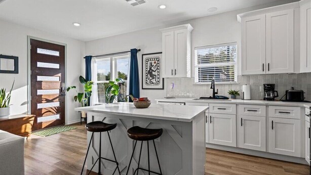 A modern kitchen with white cabinets, a central island with stools, and a window with blinds.