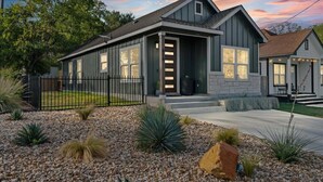 A two-story house with a grey exterior, a front porch, and a landscaped garden with rocks and plants.