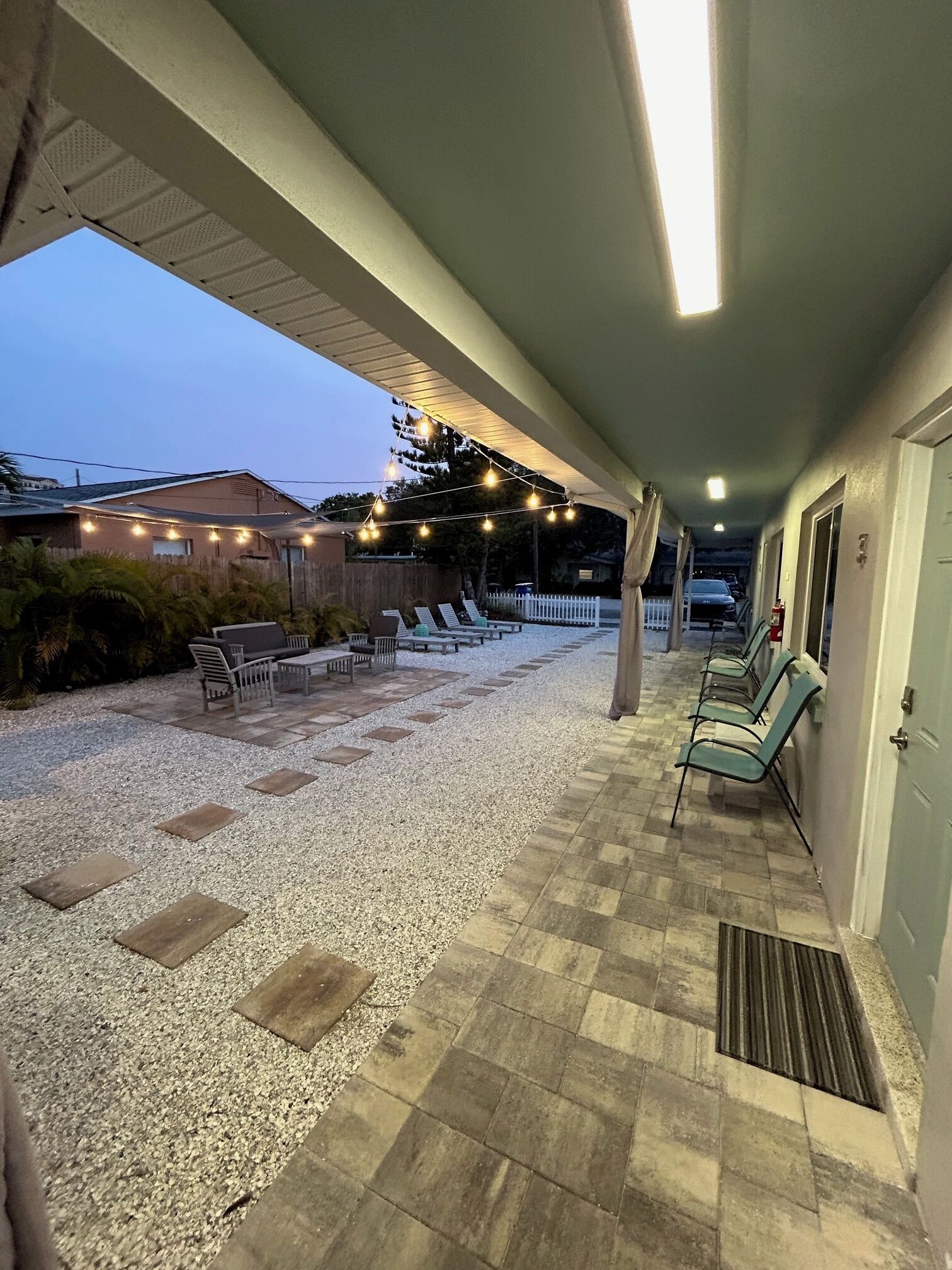 Un patio techado al aire libre con asientos, luces colgantes y un camino de grava.