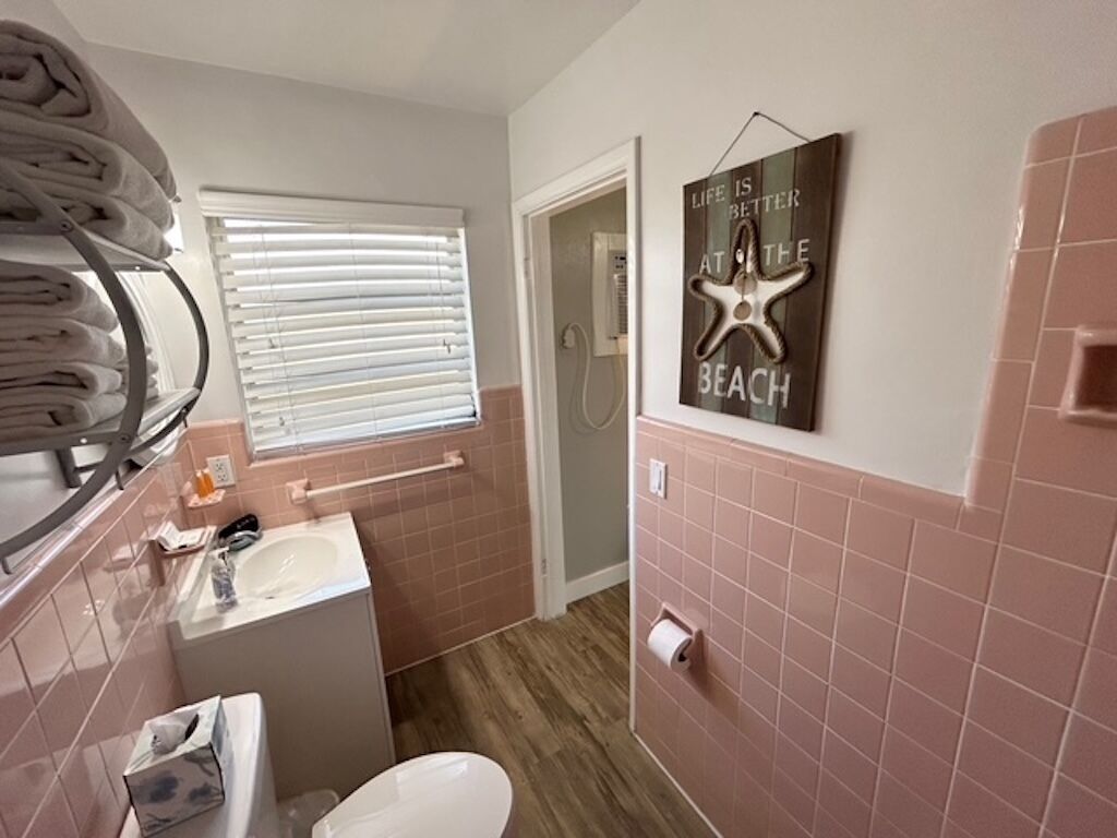 Une salle de bain avec un lavabo, des toilettes et un porte-serviettes. Il y a une décoration en forme d’étoile de mer sur le mur et une pancarte sur laquelle on peut lire : « La vie est plus belle à la plage. »